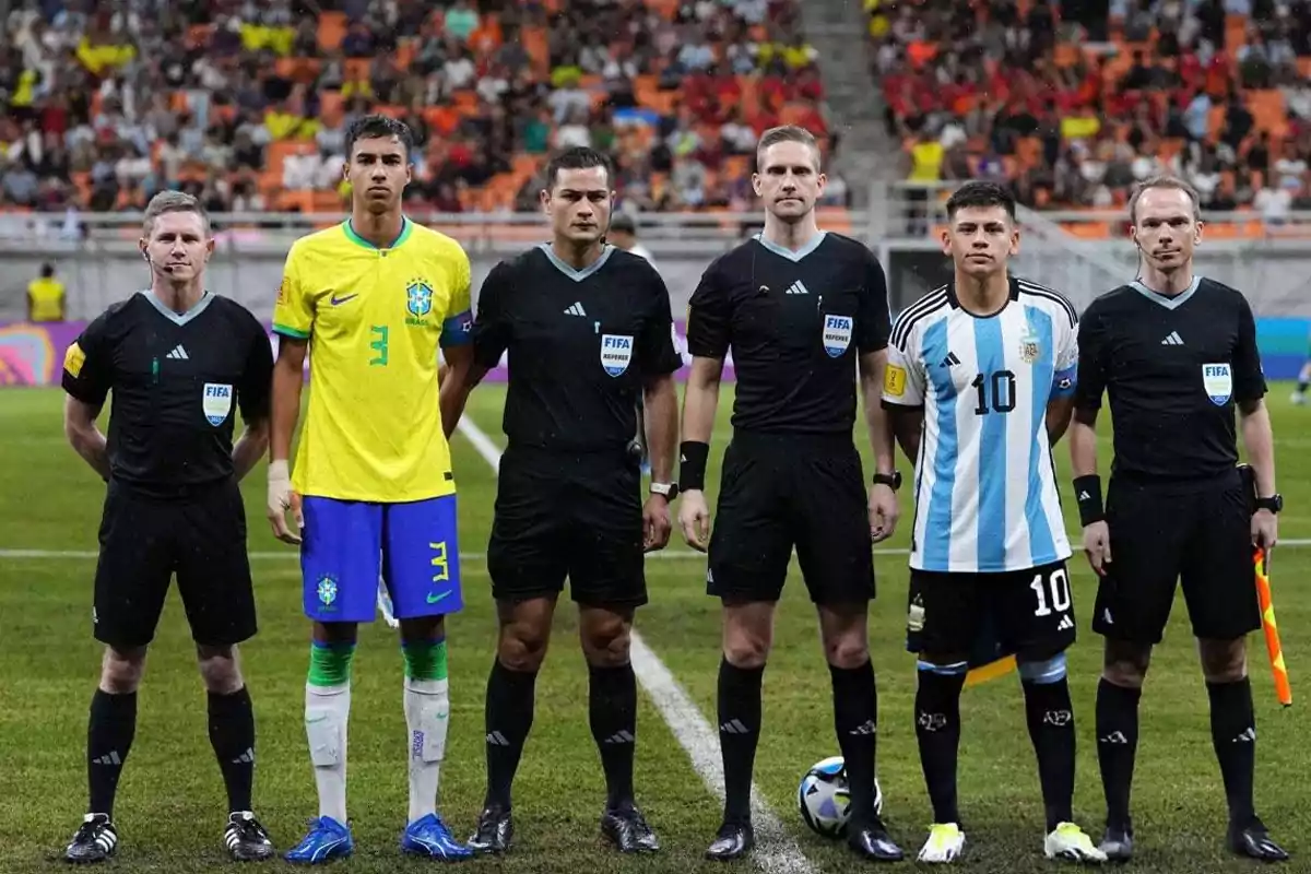 Jugadores de Brasil y Argentina posan junto a los árbitros antes de un partido de fútbol en un estadio lleno de público