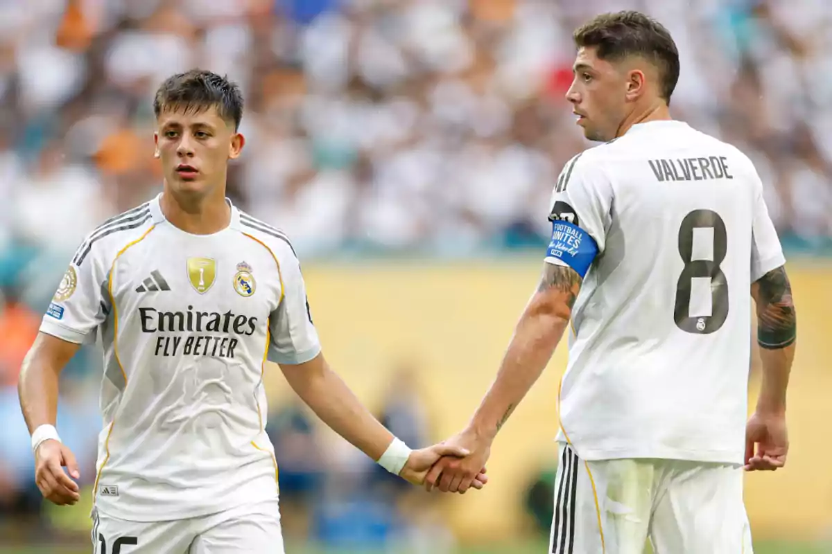 Two Real Madrid players in white uniforms hold hands on the field during a soccer match. Two Real Madrid players in white uniforms hold hands on the field during a soccer match.