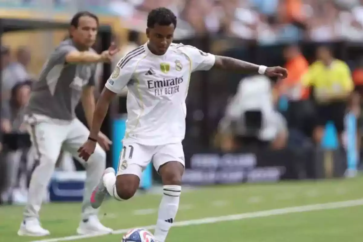 Futbolista del Real Madrid a punto de golpear el balón durante un partido con un entrenador dando indicaciones al fondo Futbolista del Real Madrid a punto de golpear el balón durante un partido con un entrenador dando indicaciones al fondo