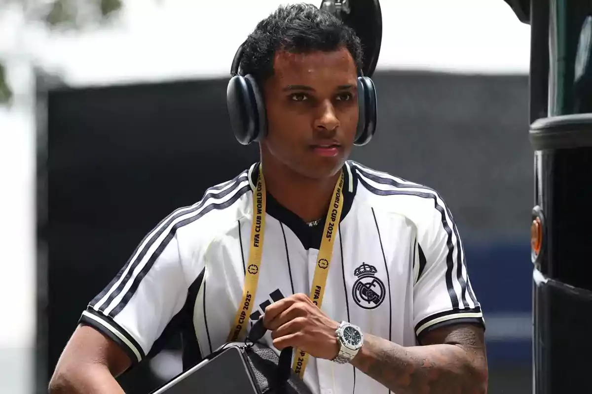 Soccer player with large headphones, a Real Madrid jersey, and a yellow armband, holding a black bag next to a bus Soccer player with large headphones, a Real Madrid jersey, and a yellow armband, holding a black bag next to a bus