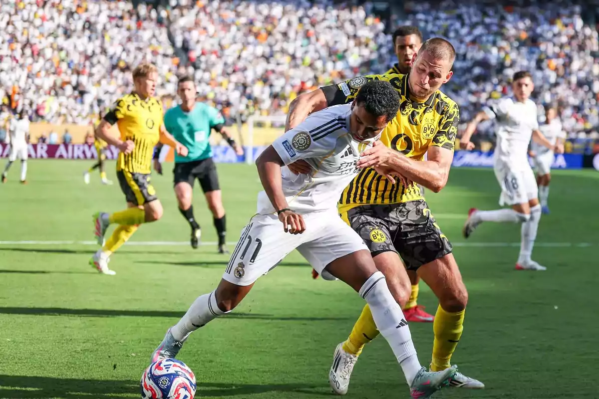 Dos futbolistas disputan el balón durante un partido entre Real Madrid y Borussia Dortmund con el estadio lleno de aficionados al fondo Dos futbolistas disputan el balón durante un partido entre Real Madrid y Borussia Dortmund con el estadio lleno de aficionados al fondo