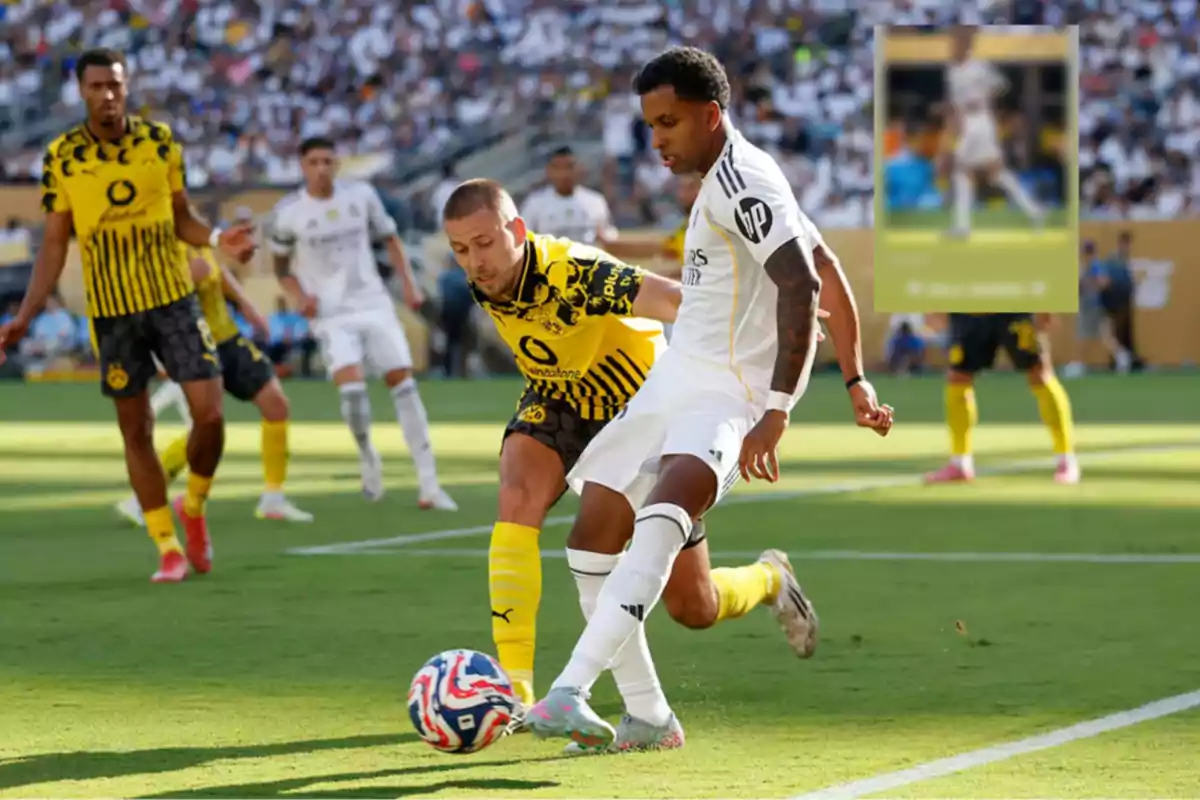 Dos futbolistas disputan el balón durante un partido entre equipos con uniformes blanco y amarillo con negro en un estadio lleno de espectadores.
