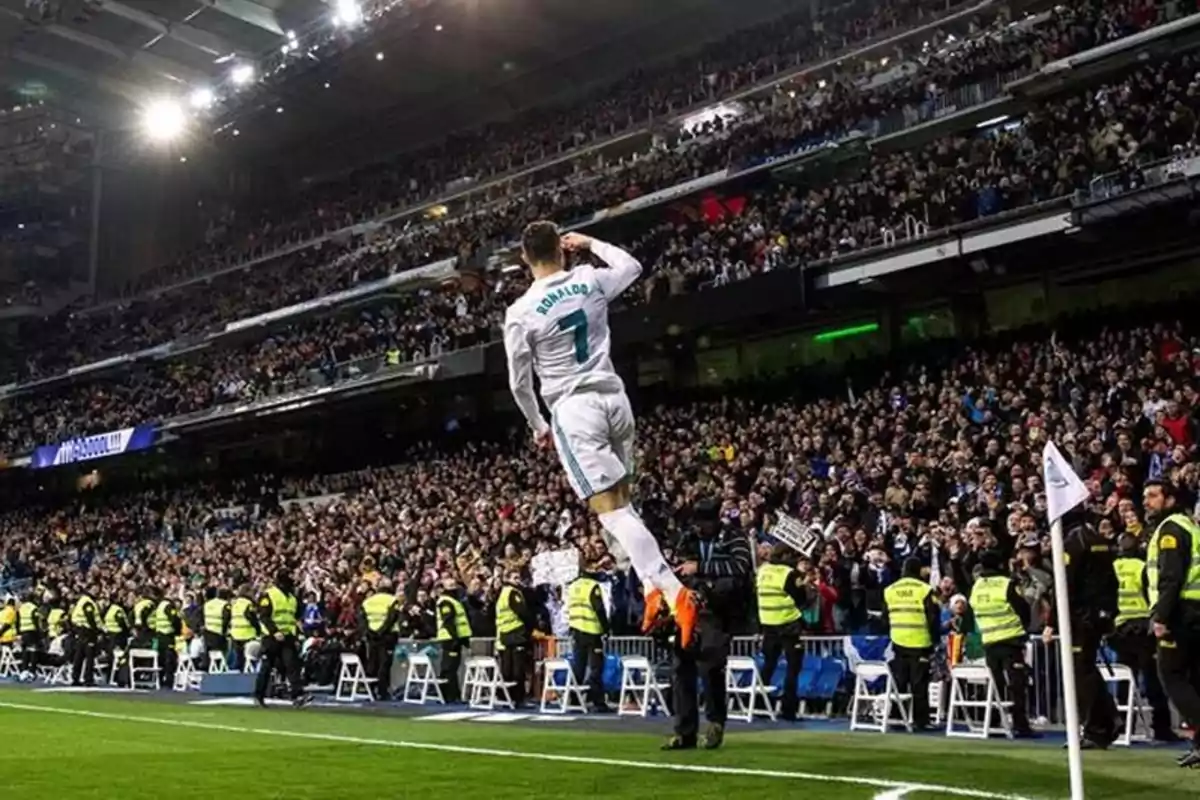 Futbolista celebrando un gol saltando cerca del banderín de córner en un estadio lleno de aficionados y personal de seguridad Futbolista celebrando un gol saltando cerca del banderín de córner en un estadio lleno de aficionados y personal de seguridad