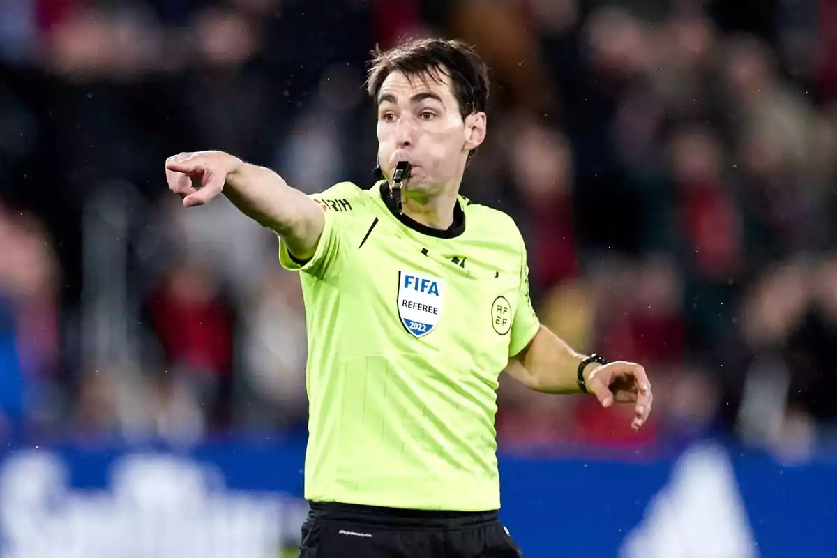 Soccer referee in a yellow uniform pointing with his arm while holding a whistle in his mouth during a match Soccer referee in a yellow uniform pointing with his arm while holding a whistle in his mouth during a match
