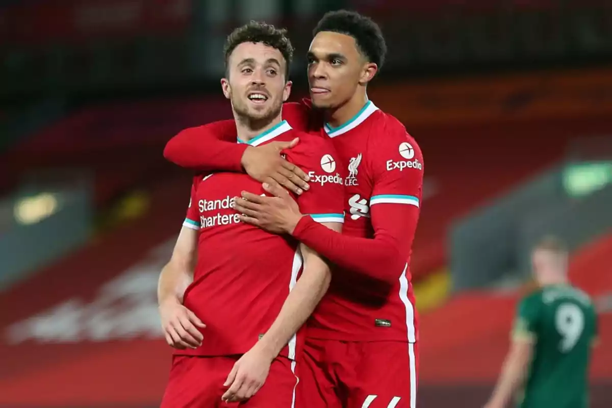 Two Liverpool footballers celebrate a goal by hugging on the field during a match. Two Liverpool footballers celebrate a goal by hugging on the field during a match.
