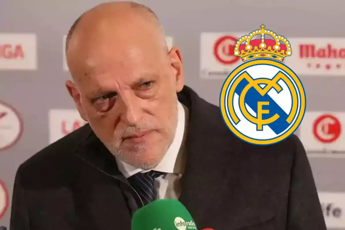 Hombre calvo de traje en una rueda de prensa con el escudo del Real Madrid superpuesto a la derecha