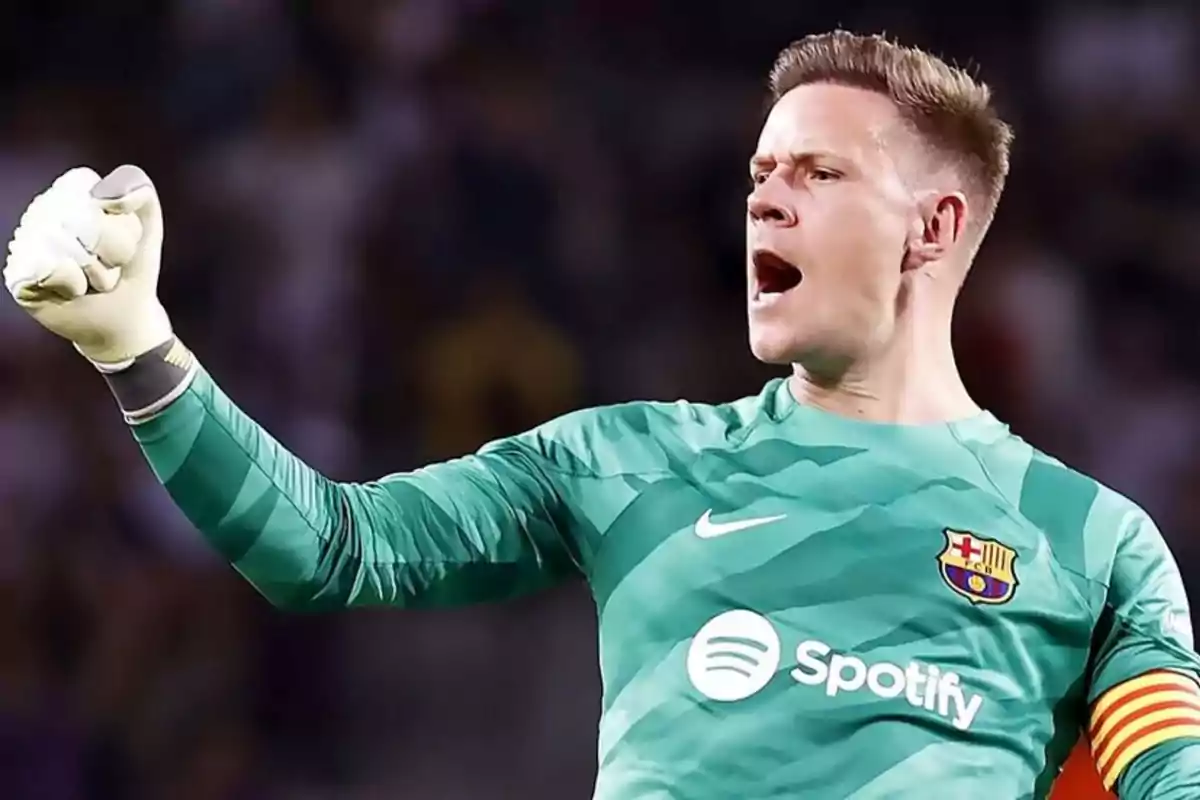 Portero del FC Barcelona celebrando con el puño en alto durante un partido, vistiendo uniforme verde y brazalete de capitán Portero del FC Barcelona celebrando con el puño en alto durante un partido, vistiendo uniforme verde y brazalete de capitán