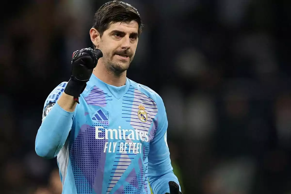 Portero del Real Madrid con uniforme azul levantando el puño derecho y expresión seria durante un partido de fútbol Portero del Real Madrid con uniforme azul levantando el puño derecho y expresión seria durante un partido de fútbol