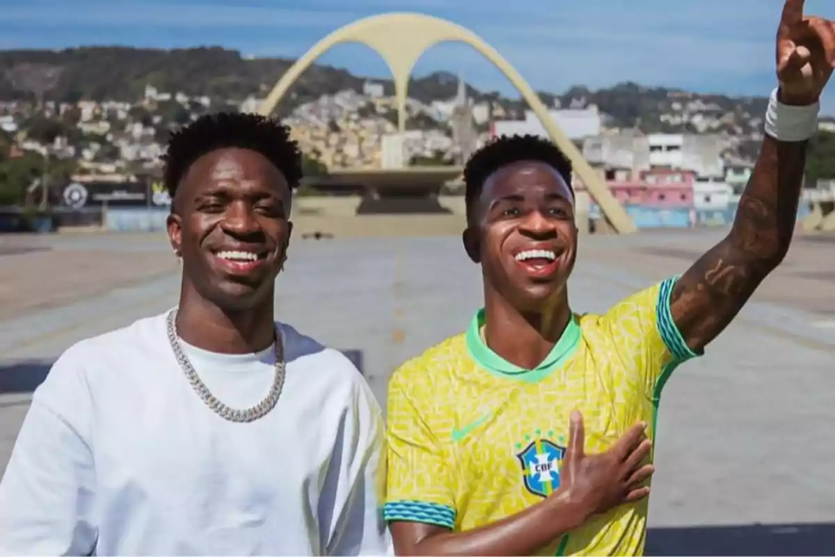 Dos personas sonríen al aire libre, una lleva una camiseta blanca y la otra una camiseta de la selección de Brasil, al fondo se observa el Sambódromo de Río de Janeiro.
