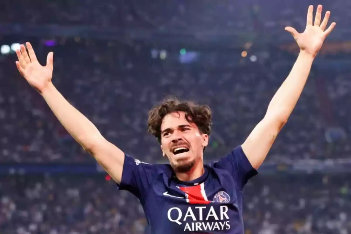 PSG player celebrating with arms raised in a stadium full of fans PSG player celebrating with arms raised in a stadium full of fans