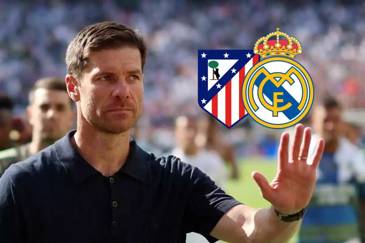 Hombre con camisa oscura levantando la mano y al fondo los escudos del Atlético de Madrid y Real Madrid
