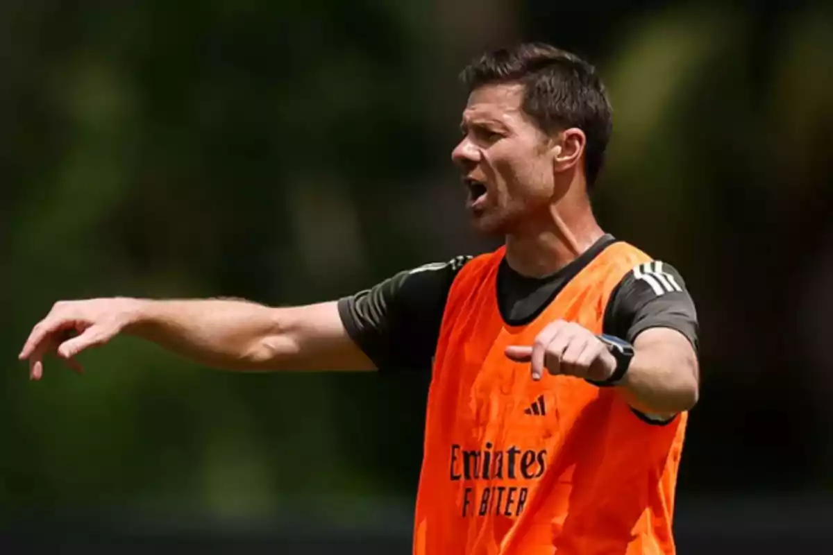 Entrenador de fútbol dando indicaciones en un campo al aire libre con chaleco naranja