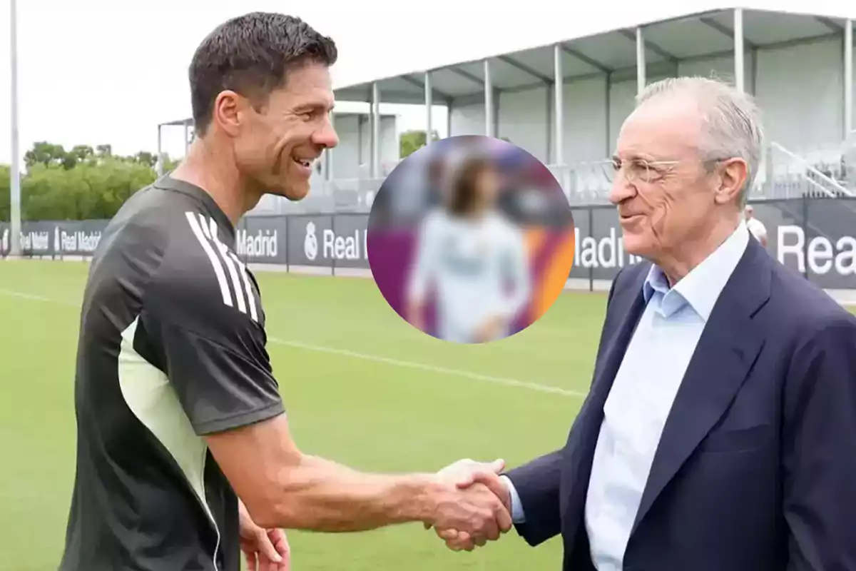 Two men shake hands on a football training field with sports facilities in the background and a blurry circle in the center of the image.