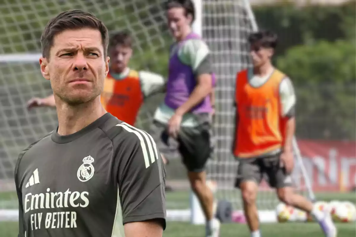 Entrenador del Real Madrid observando un entrenamiento con jugadores practicando frente a una portería en el campo de fútbol