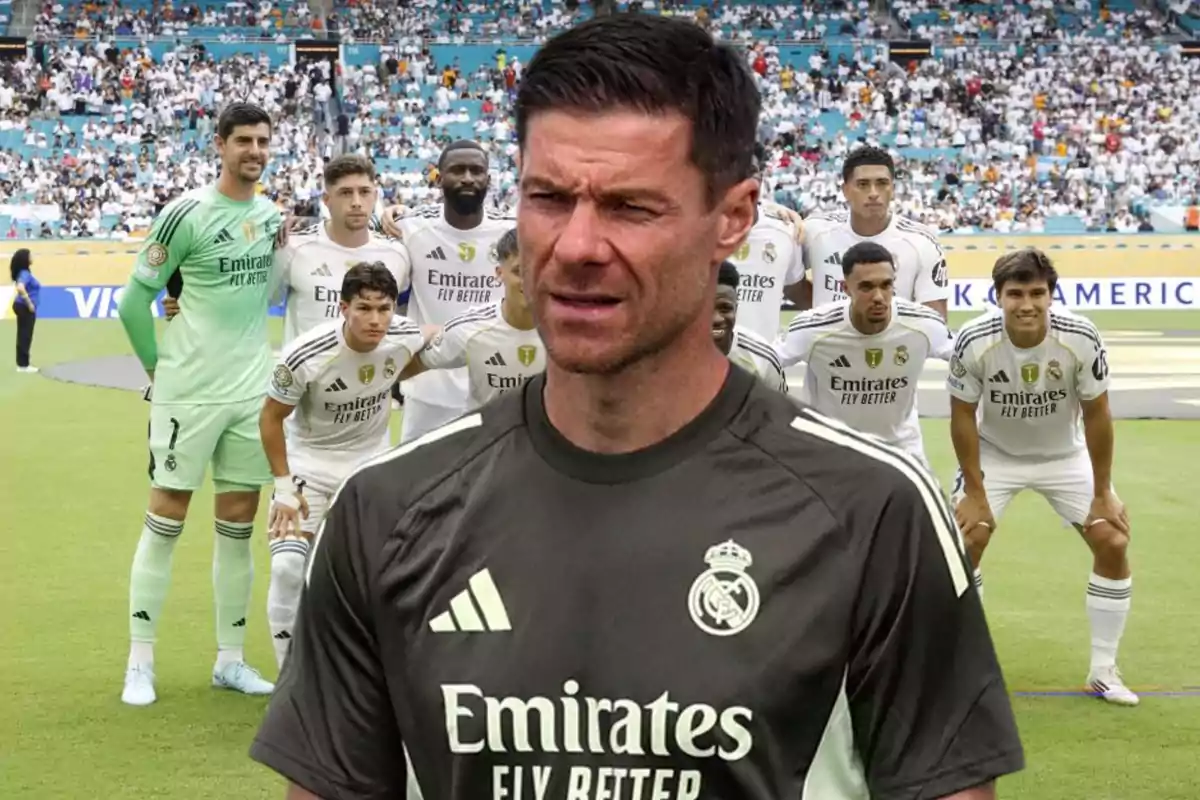 Un entrenador del Real Madrid aparece en primer plano con expresión seria mientras el equipo posa para una foto grupal en el estadio lleno de aficionados.