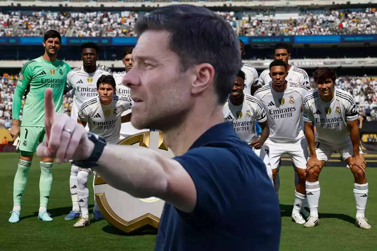 Un entrenador en primer plano da indicaciones mientras al fondo un equipo de fútbol del Real Madrid posa para la foto oficial en el estadio.