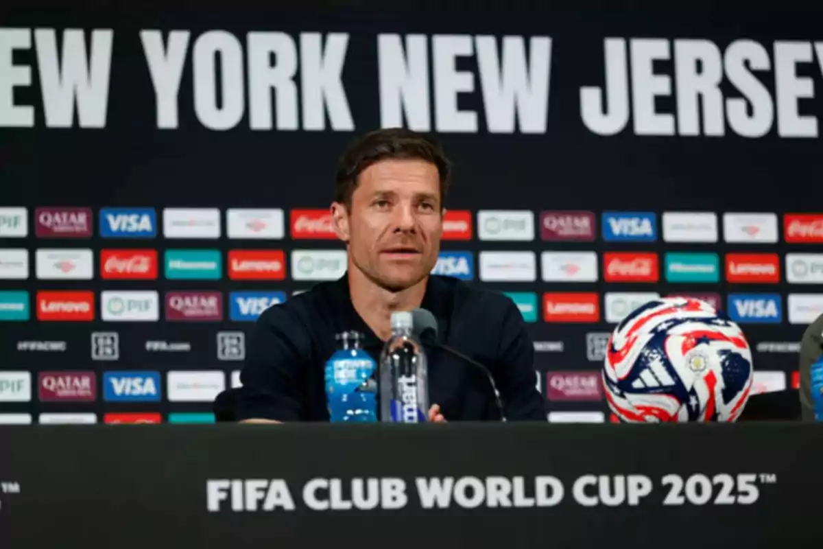 Man sitting at a press conference with a soccer ball and the text FIFA Club World Cup 2025 on the table in front of him