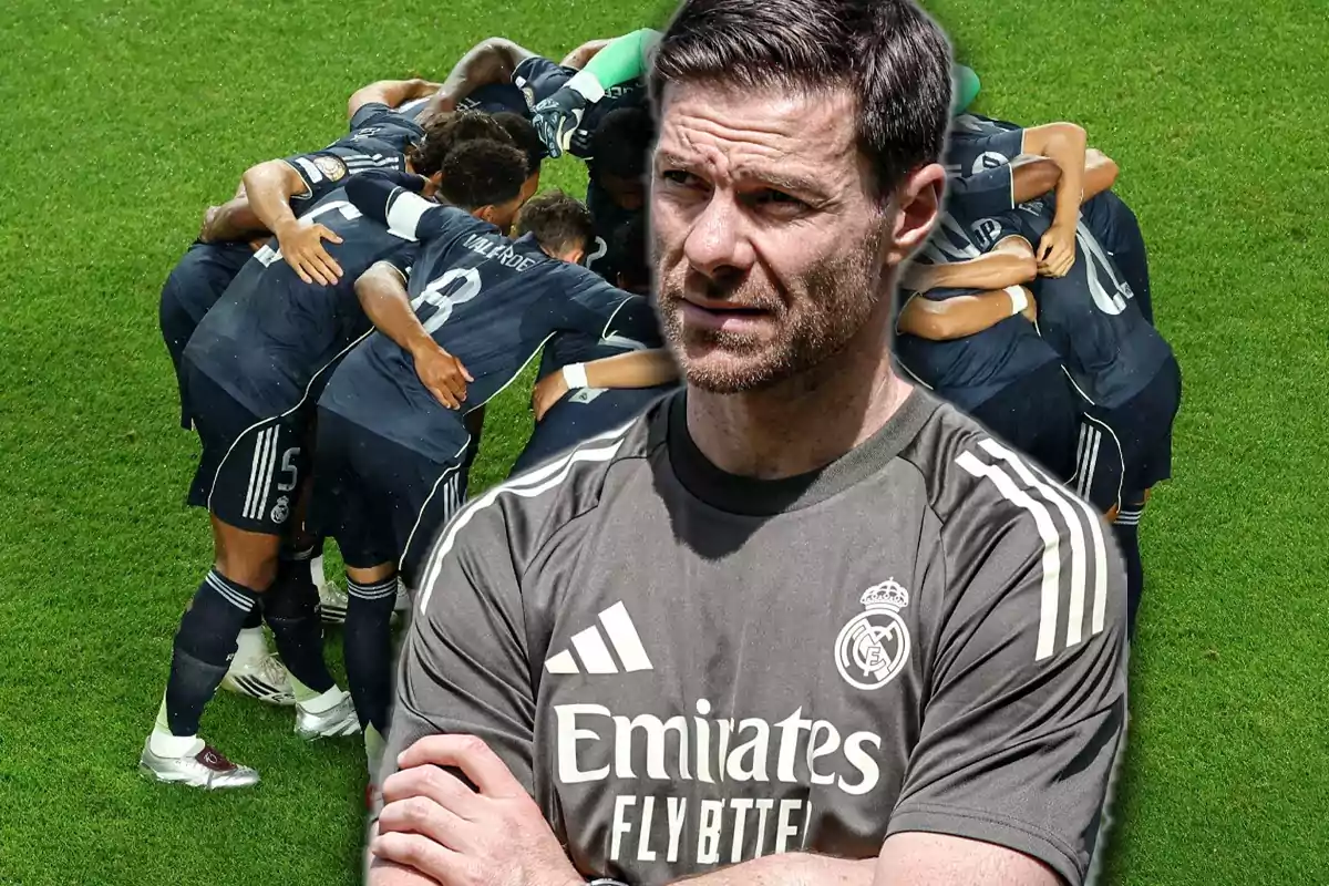 Entrenador del Real Madrid con los brazos cruzados al frente y jugadores del equipo reunidos en círculo sobre el césped al fondo