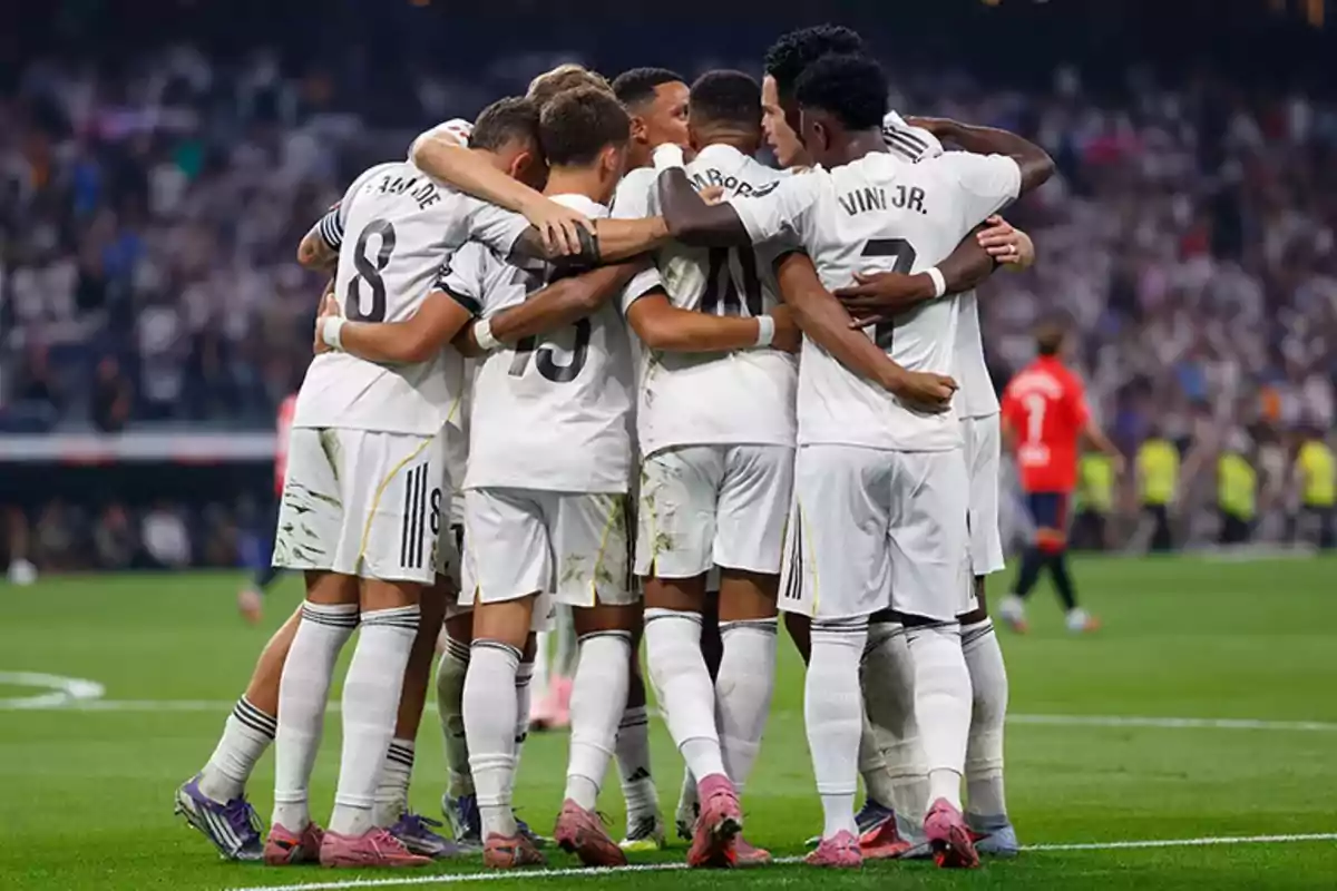 Jugadores de fútbol vestidos de blanco celebran abrazados en el campo durante un partido Jugadores de fútbol vestidos de blanco celebran abrazados en el campo durante un partido