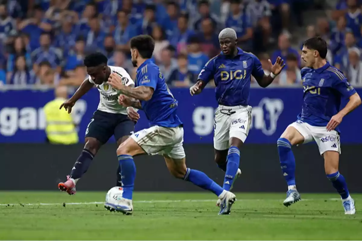 Cuatro futbolistas disputan el balón durante un partido de fútbol en un estadio lleno de espectadores Cuatro futbolistas disputan el balón durante un partido de fútbol en un estadio lleno de espectadores