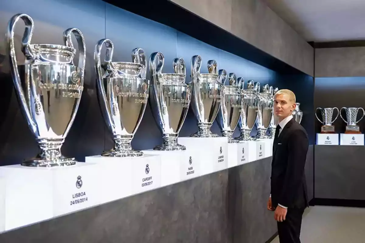 Hombre de traje observando una fila de trofeos de la Champions League exhibidos en una vitrina Hombre de traje observando una fila de trofeos de la Champions League exhibidos en una vitrina