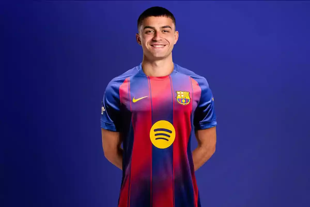 Jugador de fútbol con uniforme del FC Barcelona posando y sonriendo frente a un fondo azul Jugador de fútbol con uniforme del FC Barcelona posando y sonriendo frente a un fondo azul