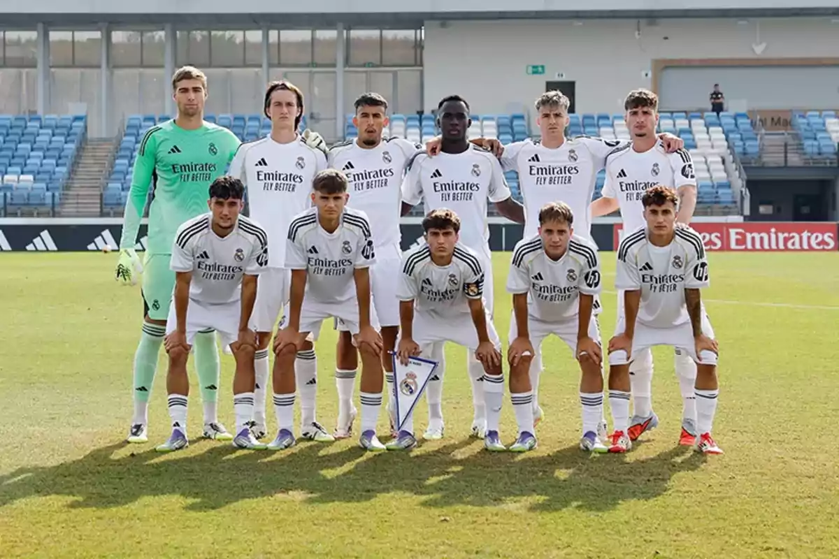 Once jugadores de fútbol con uniforme blanco posan para una foto en un estadio con gradas azules y césped verde. Once jugadores de fútbol con uniforme blanco posan para una foto en un estadio con gradas azules y césped verde.