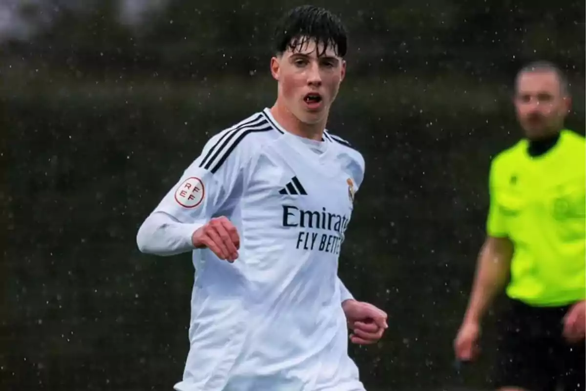 Joven futbolista con uniforme blanco del Real Madrid jugando bajo la lluvia con un árbitro de fondo Joven futbolista con uniforme blanco del Real Madrid jugando bajo la lluvia con un árbitro de fondo