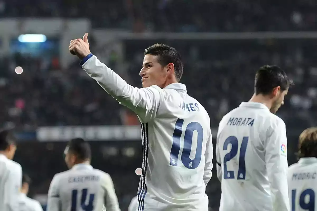 Soccer player wearing the number 10 jersey giving a thumbs up while other players in white uniforms walk beside him in a stadium full of spectators Soccer player wearing the number 10 jersey giving a thumbs up while other players in white uniforms walk beside him in a stadium full of spectators