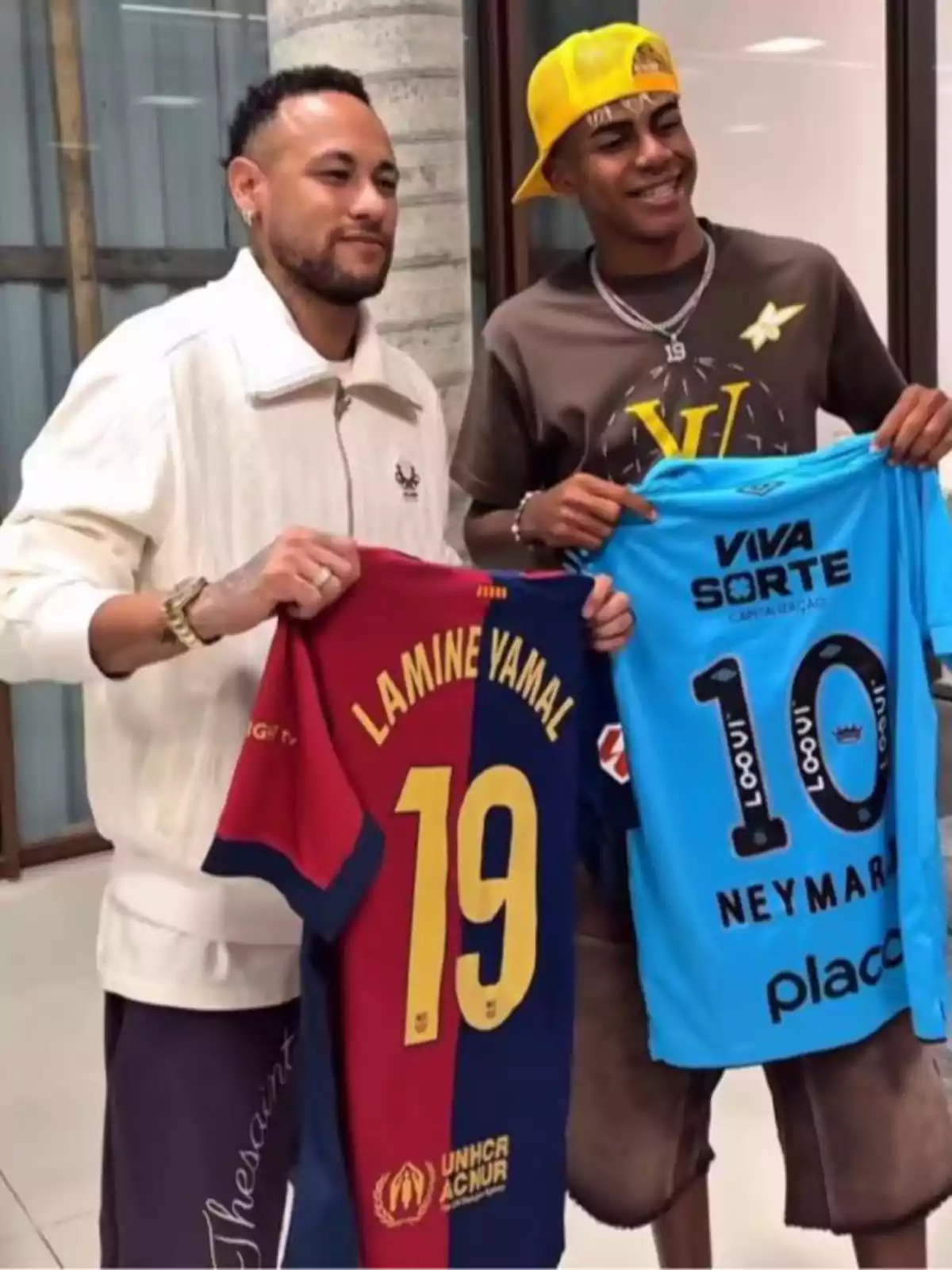 Dos personas sonríen mientras sostienen camisetas de fútbol, una del Barcelona con el nombre Lamine Yamal y el número 19, y otra azul con el nombre Neymar y el número 10 Dos personas sonríen mientras sostienen camisetas de fútbol, una del Barcelona con el nombre Lamine Yamal y el número 19, y otra azul con el nombre Neymar y el número 10