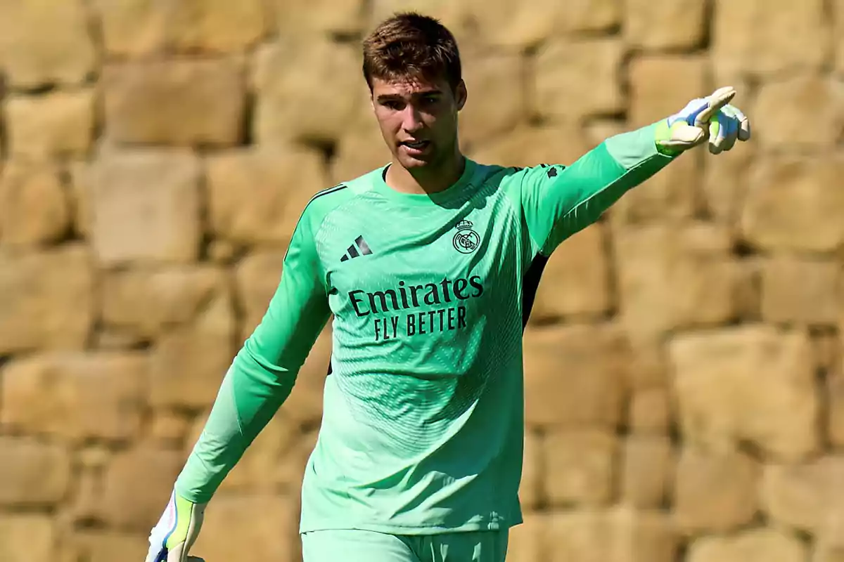 Real Madrid goalkeeper in a green uniform pointing with his right arm during a training session in front of a stone wall Real Madrid goalkeeper in a green uniform pointing with his right arm during a training session in front of a stone wall