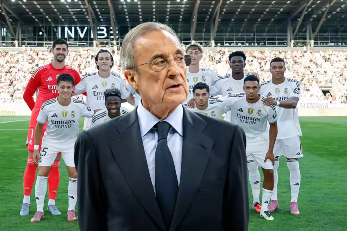 A man in a suit is standing in front of a group of players in white uniforms in a stadium full of spectators.