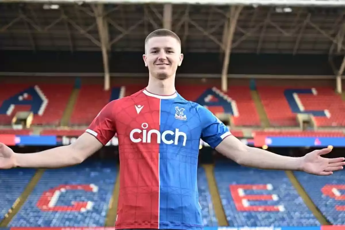 Jugador de fútbol con los brazos extendidos posando en un estadio con gradas rojas y azules y vistiendo un uniforme mitad rojo y mitad azul Jugador de fútbol con los brazos extendidos posando en un estadio con gradas rojas y azules y vistiendo un uniforme mitad rojo y mitad azul