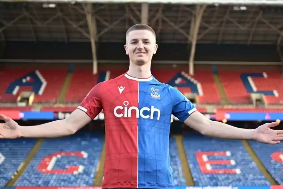 Jugador de fútbol con los brazos extendidos usando un uniforme mitad rojo y mitad azul en un estadio vacío Jugador de fútbol con los brazos extendidos usando un uniforme mitad rojo y mitad azul en un estadio vacío