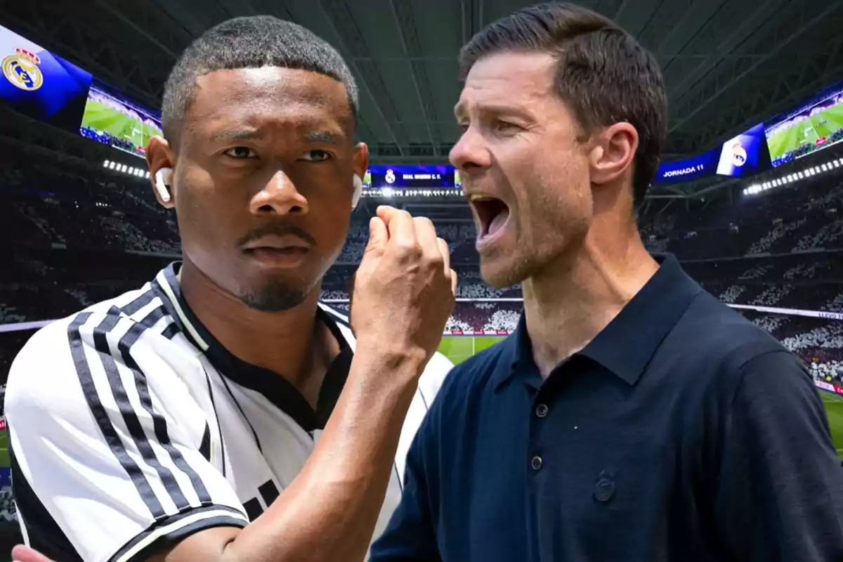 Two men in a soccer stadium, one wearing a black and white uniform and the other in a dark jersey, with screens and a crowd in the background