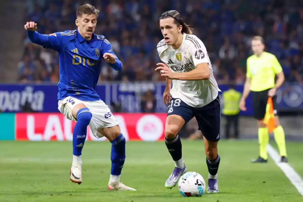 Two players fight for the ball during a match while a referee watches the play from the back of the field. Two players fight for the ball during a match while a referee watches the play from the back of the field.