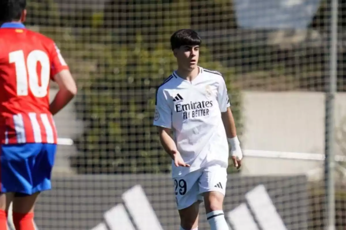 Dos futbolistas en un campo de juego uno con uniforme blanco del Real Madrid y otro con uniforme rojo y blanco del Atlético de Madrid Dos futbolistas en un campo de juego uno con uniforme blanco del Real Madrid y otro con uniforme rojo y blanco del Atlético de Madrid