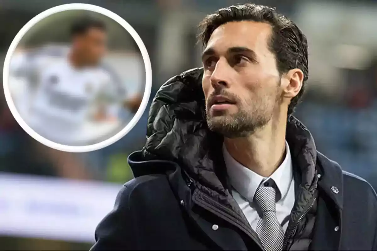 Hombre con barba y cabello corto vestido con traje y abrigo oscuro mirando hacia la izquierda con una imagen borrosa de un futbolista en el fondo dentro de un círculo blanco