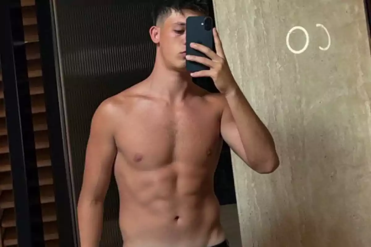 Shirtless young man taking a selfie in front of a mirror with his phone covering his face Shirtless young man taking a selfie in front of a mirror with his phone covering his face