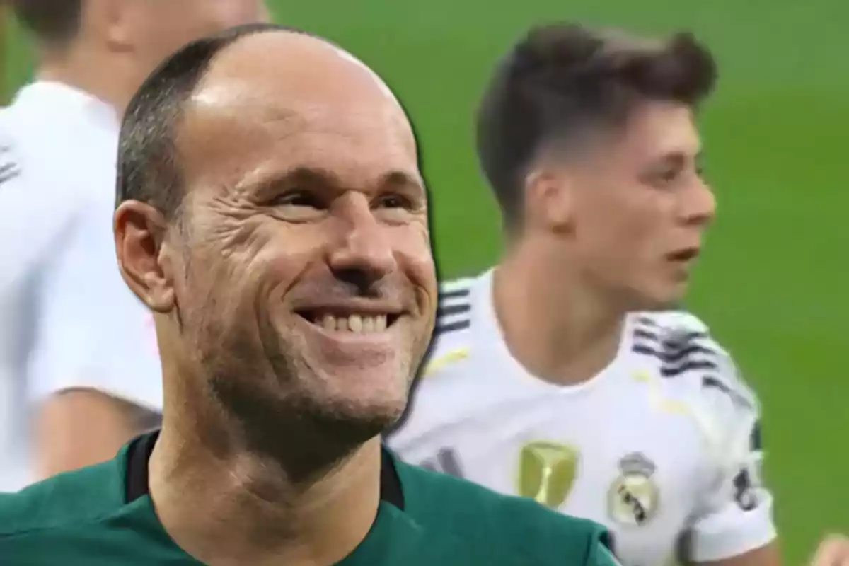 A smiling referee in the foreground with a Real Madrid player out of focus in the background on a soccer field