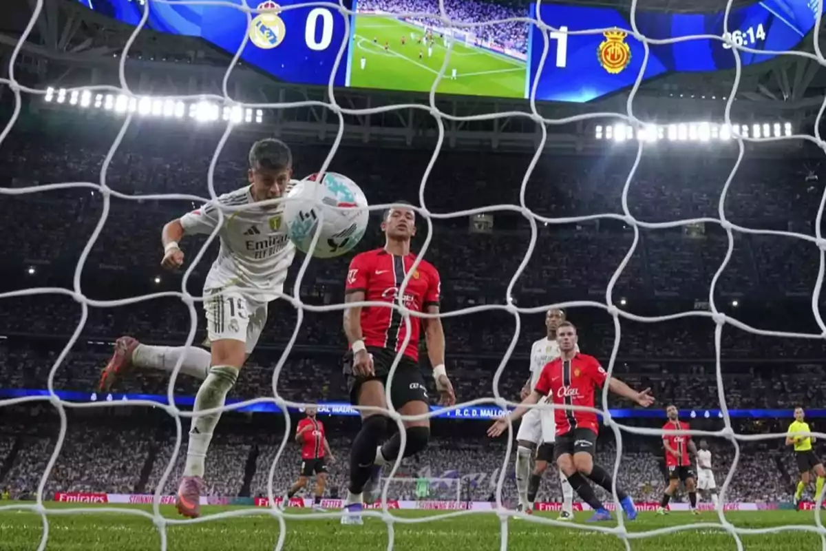 A Real Madrid player heads the ball toward the goal while several Mallorca players watch the play in a packed stadium and the scoreboard shows the visiting team in the lead. A Real Madrid player heads the ball toward the goal while several Mallorca players watch the play in a packed stadium and the scoreboard shows the visiting team in the lead.