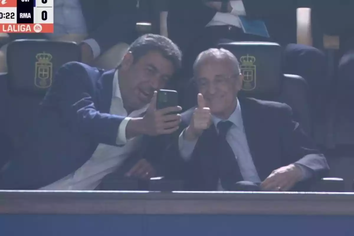 Dos hombres vestidos de traje se toman una selfie en un estadio mientras uno de ellos sonríe y levanta el pulgar en señal de aprobación Dos hombres vestidos de traje se toman una selfie en un estadio mientras uno de ellos sonríe y levanta el pulgar en señal de aprobación