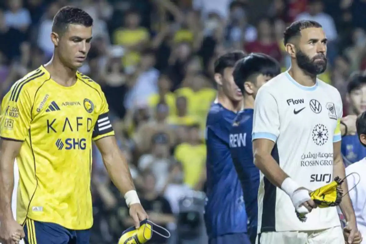 Two players wearing different team uniforms walk together on the field holding pennants while the crowd watches from the stands. Two players wearing different team uniforms walk together on the field holding pennants while the crowd watches from the stands.