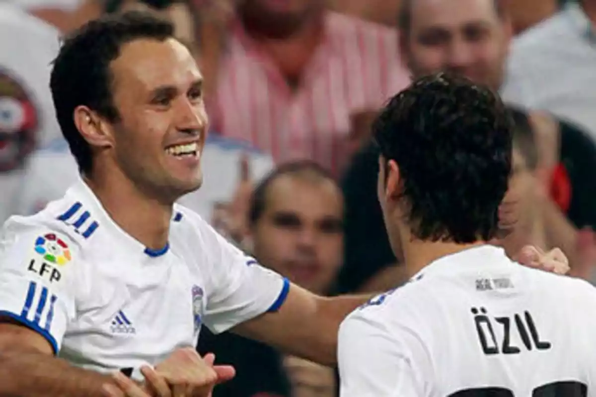 Two Real Madrid players celebrate a goal during a soccer match, one of them smiling while hugging his teammate who has the name Özil on his jersey. Two Real Madrid players celebrate a goal during a soccer match, one of them smiling while hugging his teammate who has the name Özil on his jersey.