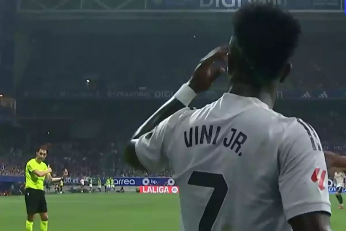 Futbolista con la camiseta de Vini Jr. número 7 celebrando en un estadio mientras un árbitro observa a lo lejos Futbolista con la camiseta de Vini Jr. número 7 celebrando en un estadio mientras un árbitro observa a lo lejos