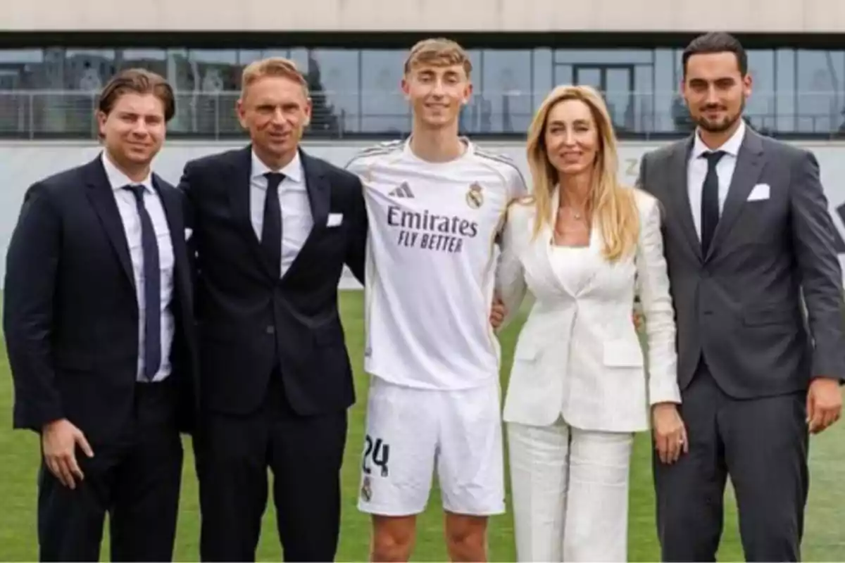 Cinco personas posan juntas en un campo de fútbol, cuatro de ellas visten traje formal y una lleva el uniforme del Real Madrid Cinco personas posan juntas en un campo de fútbol, cuatro de ellas visten traje formal y una lleva el uniforme del Real Madrid