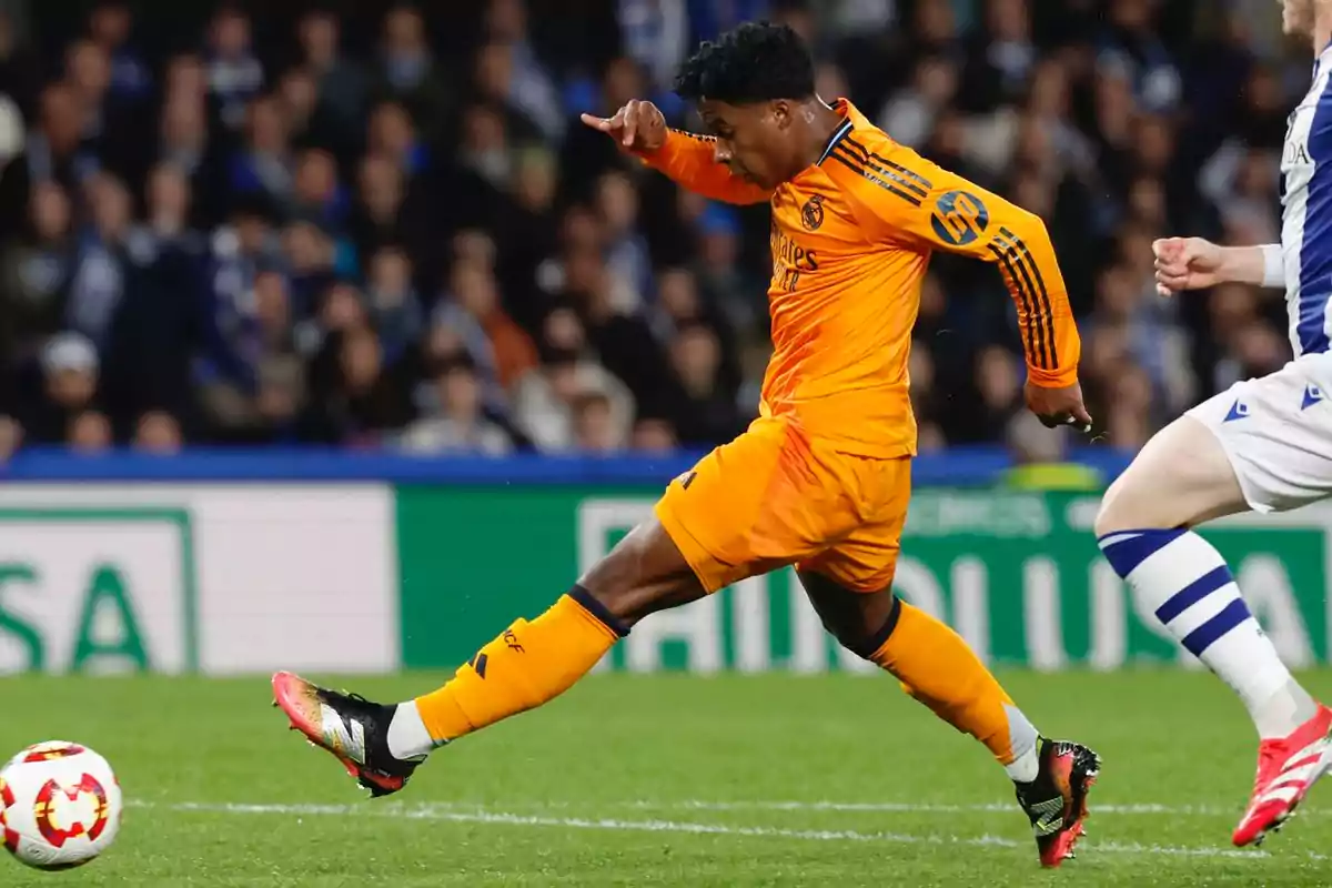 Futbolista con uniforme naranja del Real Madrid pateando el balón durante un partido Futbolista con uniforme naranja del Real Madrid pateando el balón durante un partido