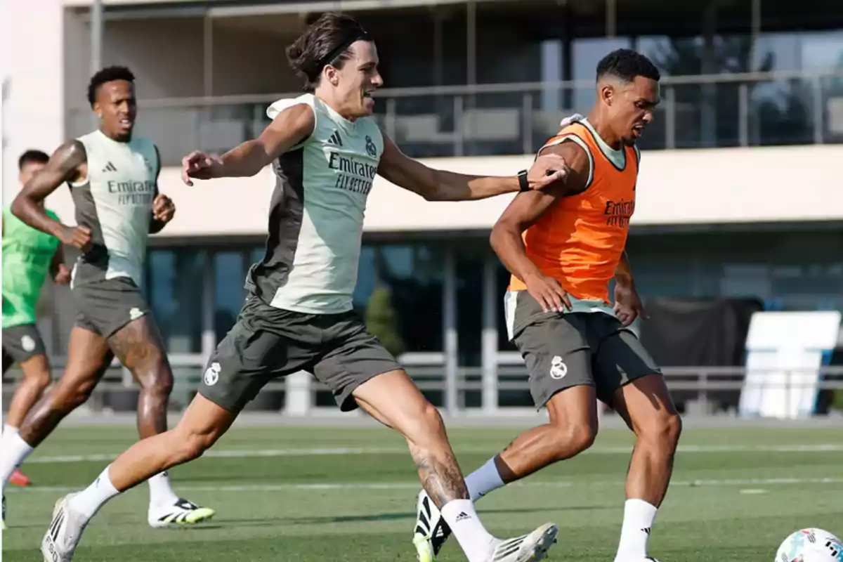 Jugadores del Real Madrid entrenando en el campo mientras uno intenta quitarle el balón a otro que lleva un peto naranja Jugadores del Real Madrid entrenando en el campo mientras uno intenta quitarle el balón a otro que lleva un peto naranja