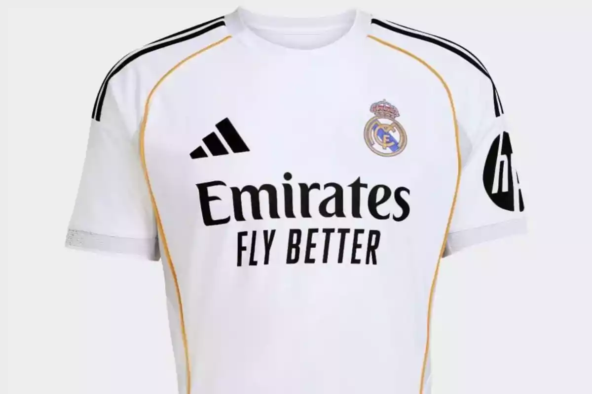 Camiseta blanca del Real Madrid con detalles en dorado y negro, logotipo de Adidas, escudo del club y patrocinadores en el frente y la manga Camiseta blanca del Real Madrid con detalles en dorado y negro, logotipo de Adidas, escudo del club y patrocinadores en el frente y la manga