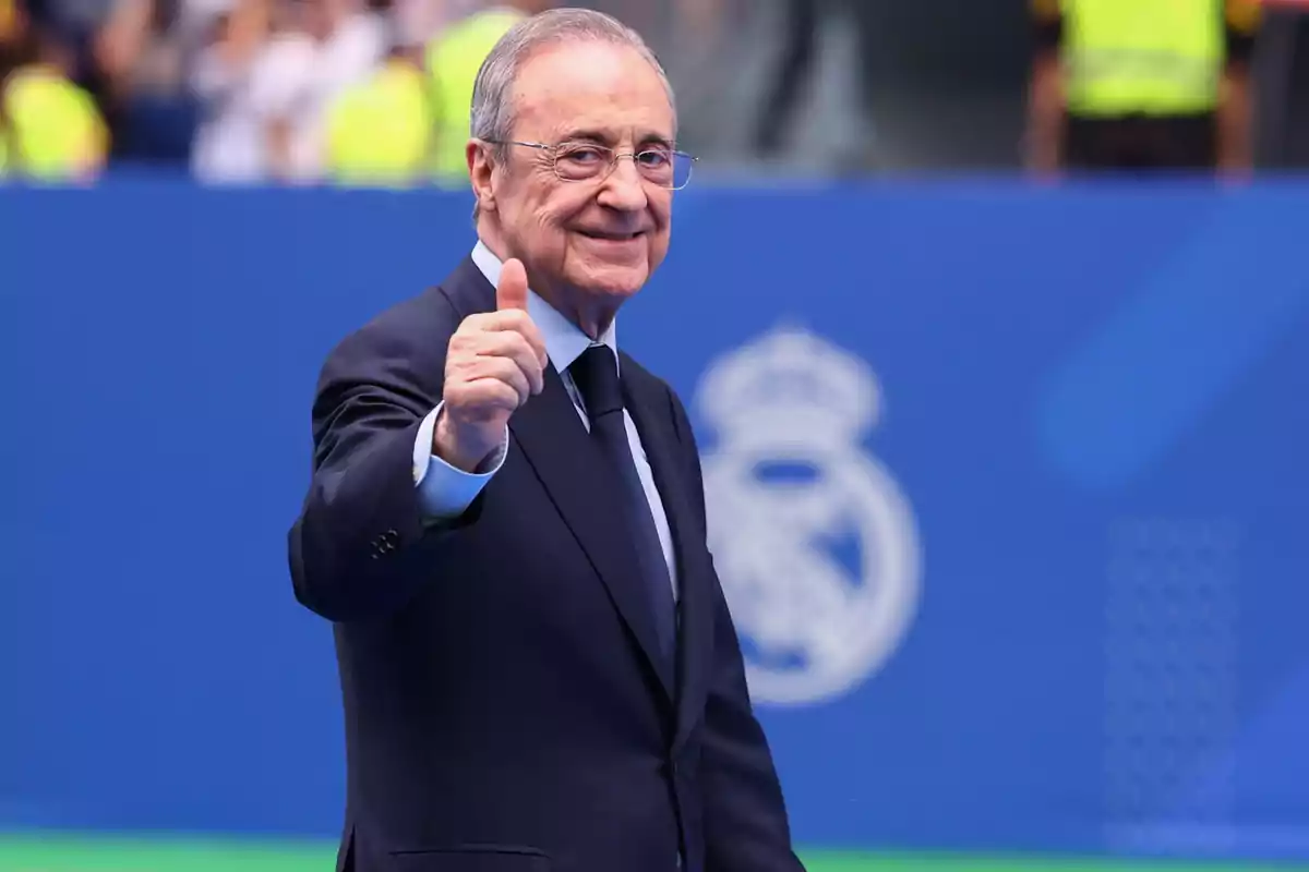 Smiling man in a suit giving a thumbs up in a stadium with a blue background Smiling man in a suit giving a thumbs up in a stadium with a blue background